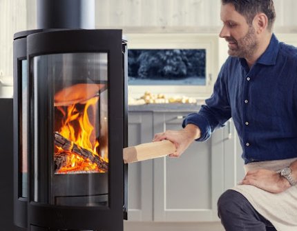 Un homme mets du bois dans le poêle scandinave